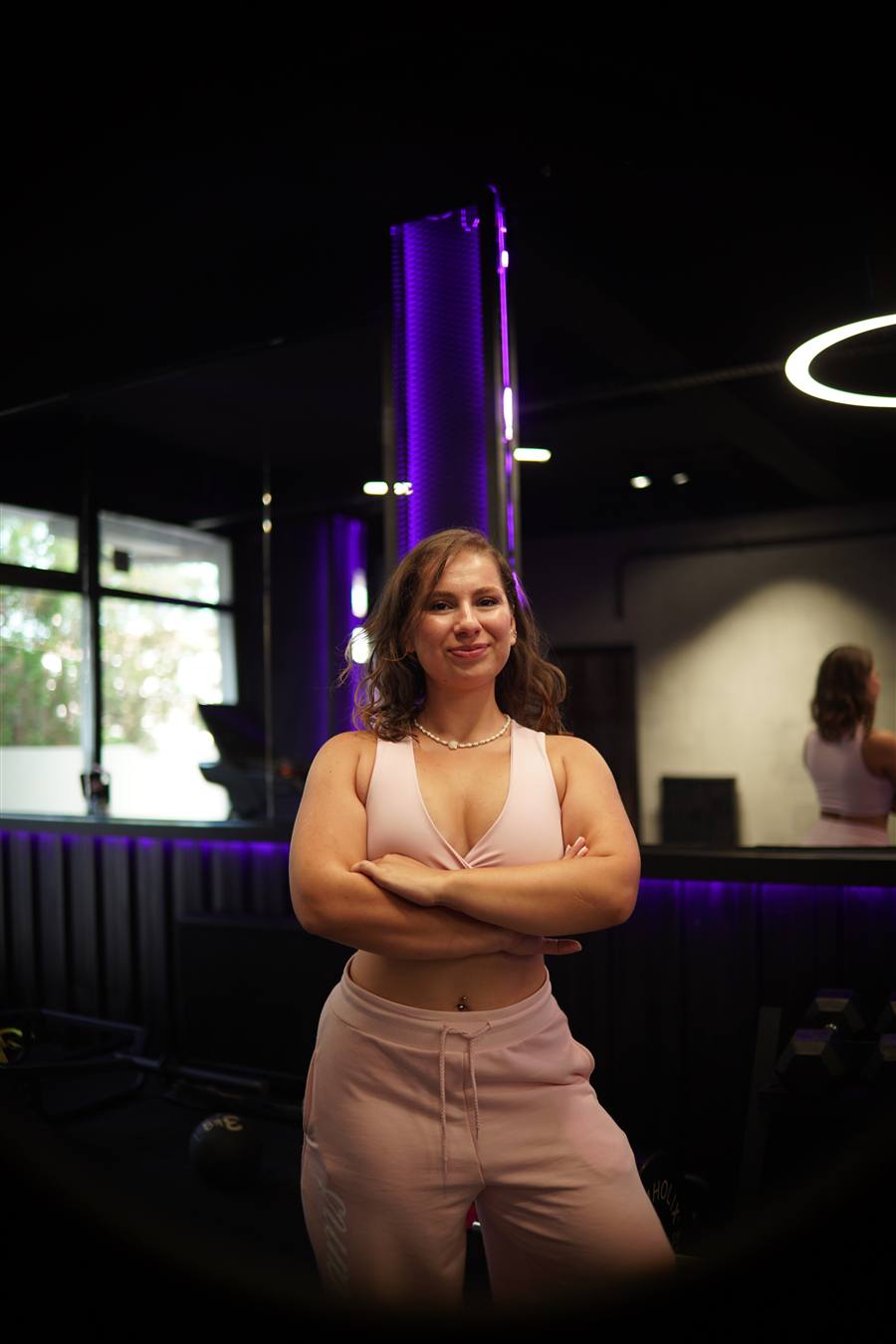 Pembe spor kıyafetli bir kadın antrenörün ACK Fitness stüdyosunda kollarını kavuşturmuş portresi